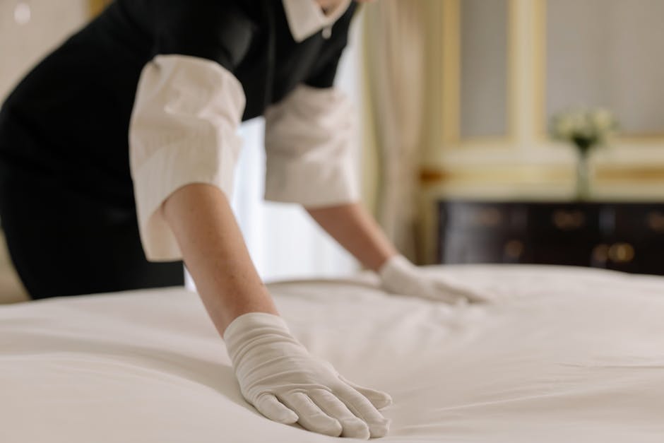 A professional cleaner from Seven Kings Carpet Cleaners, dressed in a black and white uniform, is carefully handling a white towel or cloth on a table or countertop within an elegantly decorated room.