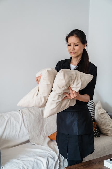 A vintage-style upholstered armchair with light wooden legs and frame, placed in a bright, minimalist room with white walls and a glossy white floor. A soft beige throw blanket is draped over the back